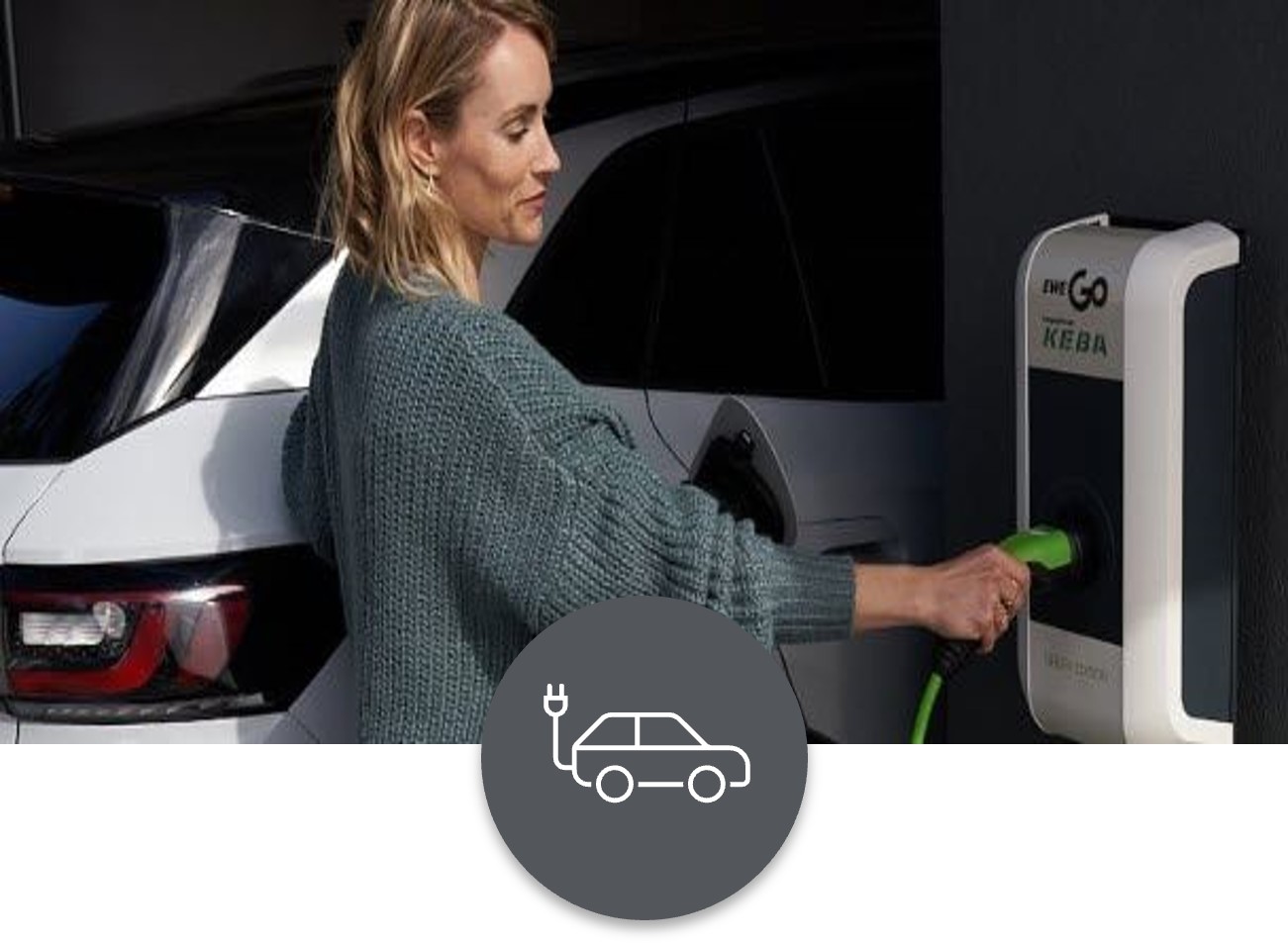 Wallbox-und-Autostrom Eine Frau mit blondem Schulterlangen Haarschnitt schließt ihr parkendes Elektrofahrzeug an einer Elektro-Ladestation an.