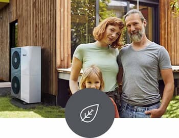 heizen-mit-waermepumpe Mutter, Vater und Tochter posieren im Garten vor ihrem Haus mit Holz-Fassade. An der Hauswand ist eine Wärmepumpe installiert.